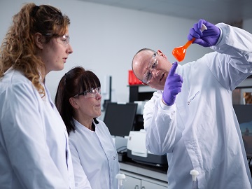 Eurofins employees examining orange coloured flask as part of testing in support of GMP contract manufacturing